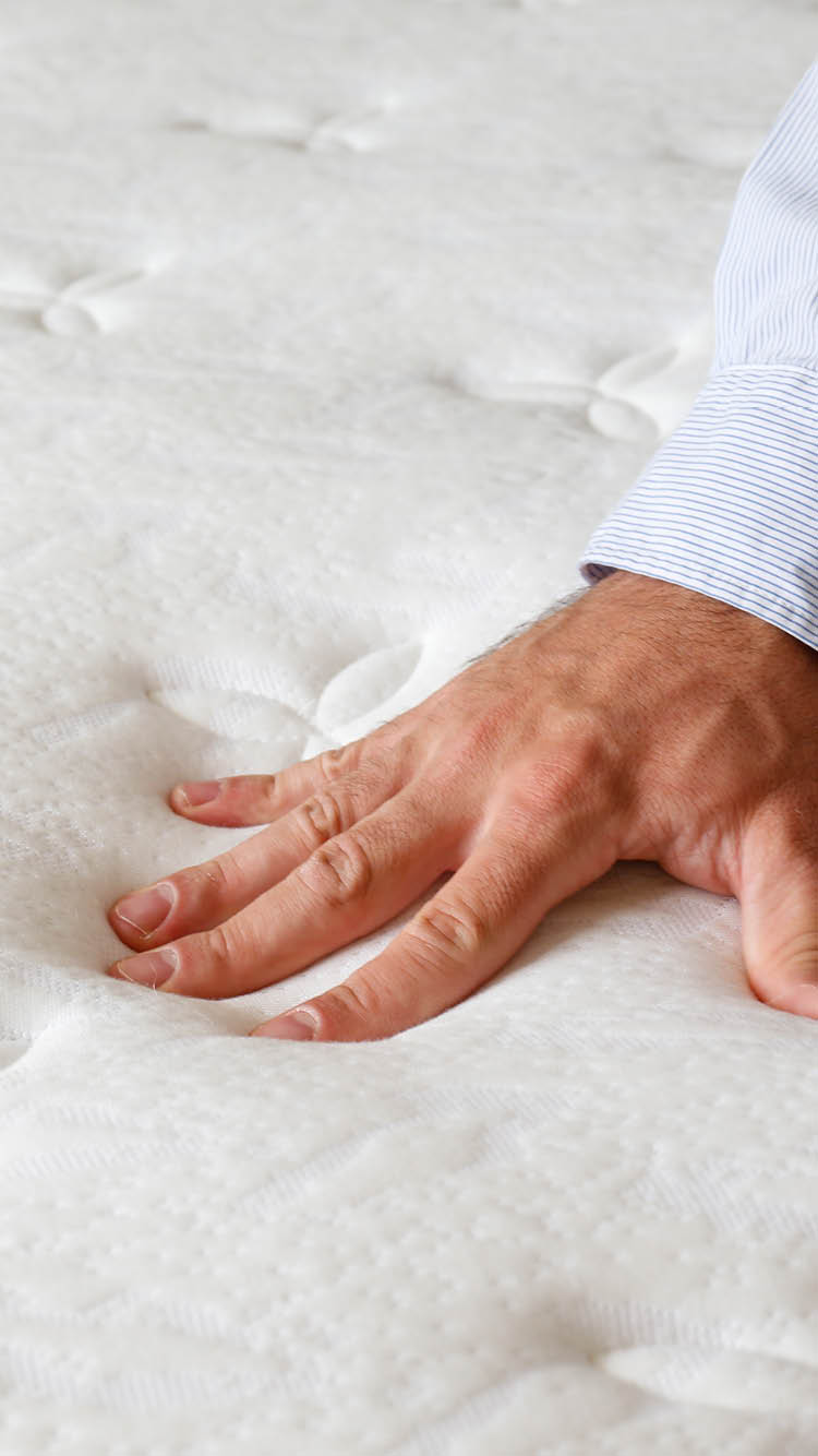 Cropped shot of man testing white orthopedic matress on firmness. Male pressing hypoallergenic foam mattresses surface to check its softness. Close up, copy space, top view, background.