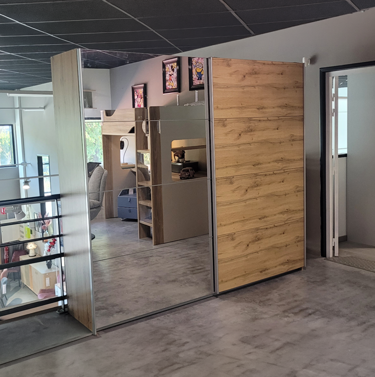 Un meuble avec une porte en miroir refl te une pi ce avec un canap , des tag res, des cadres color s accroch s au mur et un sol en b ton.  Description g n r e par IA