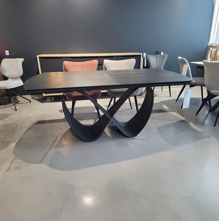Table noire moderne avec un plateau rectangulaire et un pied sculptural en forme de ruban entrelac entour e de plusieurs chaises de styles vari s dans un espace int rieur minimaliste.  Description g n r e par IA