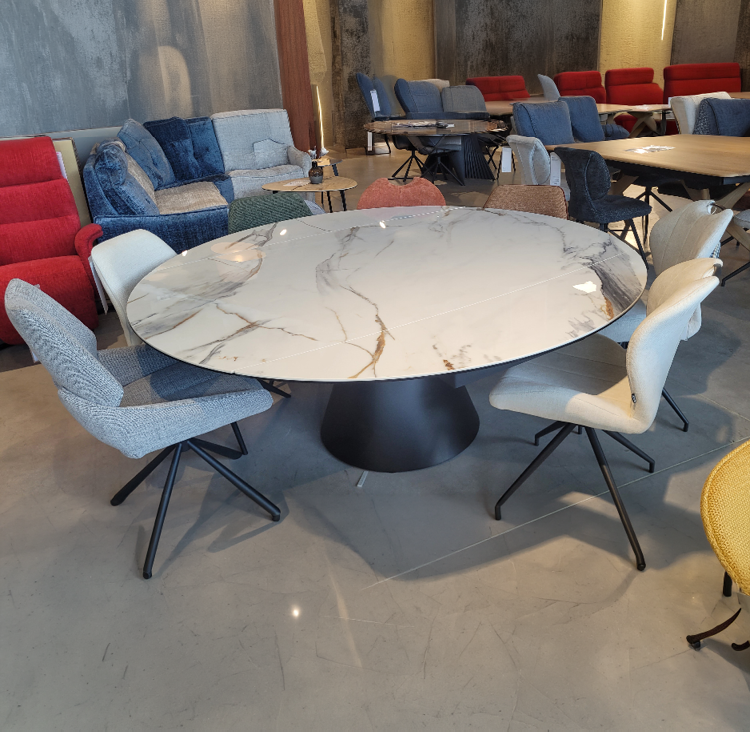 Une table ronde en marbre blanc avec six chaises modernes est plac e dans un espace int rieur lumineux avec plusieurs canap s et autres tables en arri re-plan. Description g n r e par IA