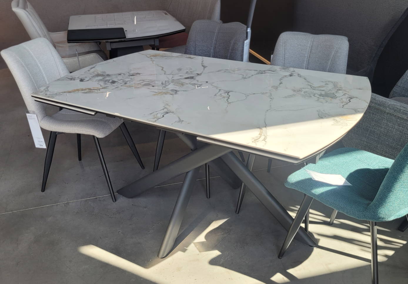 Table moderne avec plateau en marbre blanc et pieds m talliques gris entour e de plusieurs chaises de styles diff rents dans un espace int rieur lumineux. Description g n r e par IA