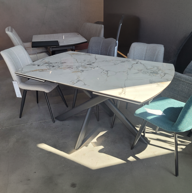 Table moderne avec plateau en marbre blanc et pieds m talliques noirs entour e de plusieurs chaises de styles et couleurs vari s dans un espace int rieur lumineux. Description g n r e par IA