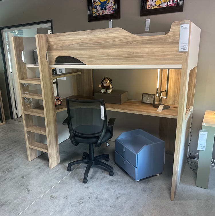 Un bureau en bois clair avec un lit mezzanine, une chaise de bureau noire, un petit meuble bleu  roulettes et une lampe pos e sur une table   c t .  Description g n r e par IA