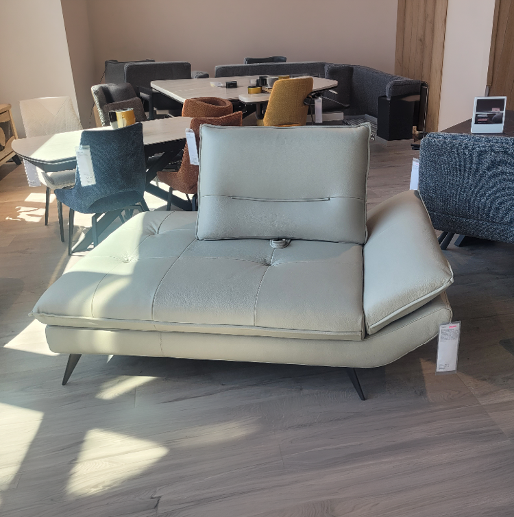 Un canap moderne en cuir beige avec un dossier ajustable est plac  dans un salon lumineux avec plusieurs chaises et tables autour.  Description g n r e par IA